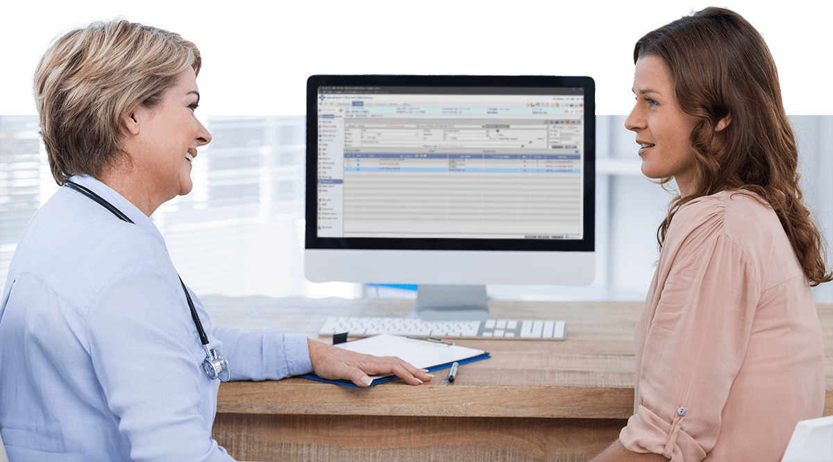 A medical provider and patient talk in front of a computer displaying medical practice management software.